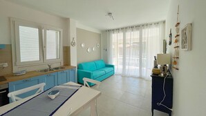 A kitchen with a sink, a dining table with chairs, a blue sofa, and a small cabinet with a lamp.