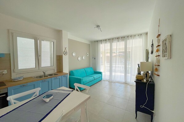 A kitchen with a sink, a dining table with chairs, a blue sofa, and a small cabinet with a lamp.