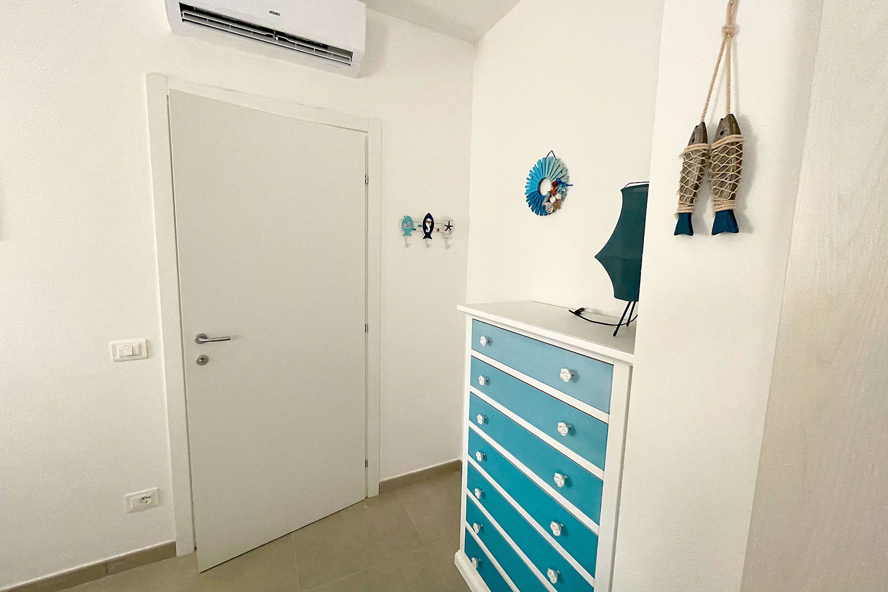 A room with a white door, a blue dresser, wall decorations, and an air conditioning unit.