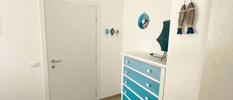A room with a white door, a blue dresser, wall decorations, and an air conditioning unit.