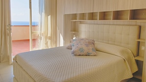 Une chambre avec un grand lit, une tête de lit et une vue sur l’extérieur, accessible par une porte coulissante.
