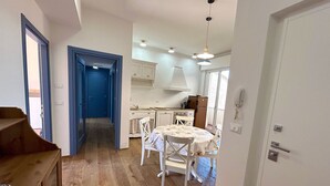 Una cocina con armarios blancos, una mesa de comedor con sillas y una puerta azul que da a otra habitación.