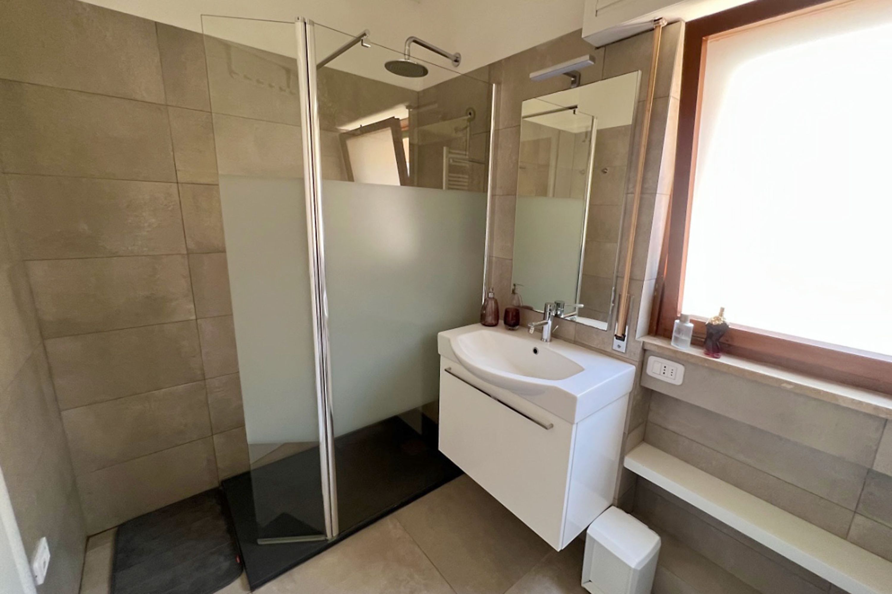 Ein modernes Badezimmer mit Duschkabine aus Glas, einem weißen Waschbecken und einem großen Spiegel.