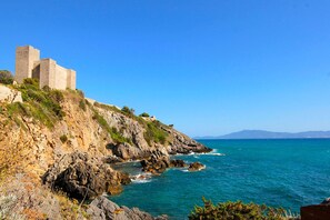 A coastal landscape with a historical stone structure on a hillside overlooking the sea. - Appartamento Blue Sea con Vista Mare (Orbetello)