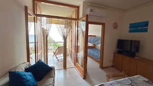 Una habitació amb sofà, llit, televisió i un balcó amb vistes.