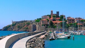 Un poble costaner amb una fortificació, una marina amb vaixells i edificis amb teulades vermelles.