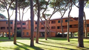A building with multiple floors, surrounded by trees and a grassy courtyard. - Appartamento Germoglio Sulla Spiaggia (Orbetello)