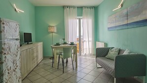 A compact living space with a dining area, a sofa, a TV, and a painting on the wall. - Appartamento Germoglio Sulla Spiaggia (Orbetello)