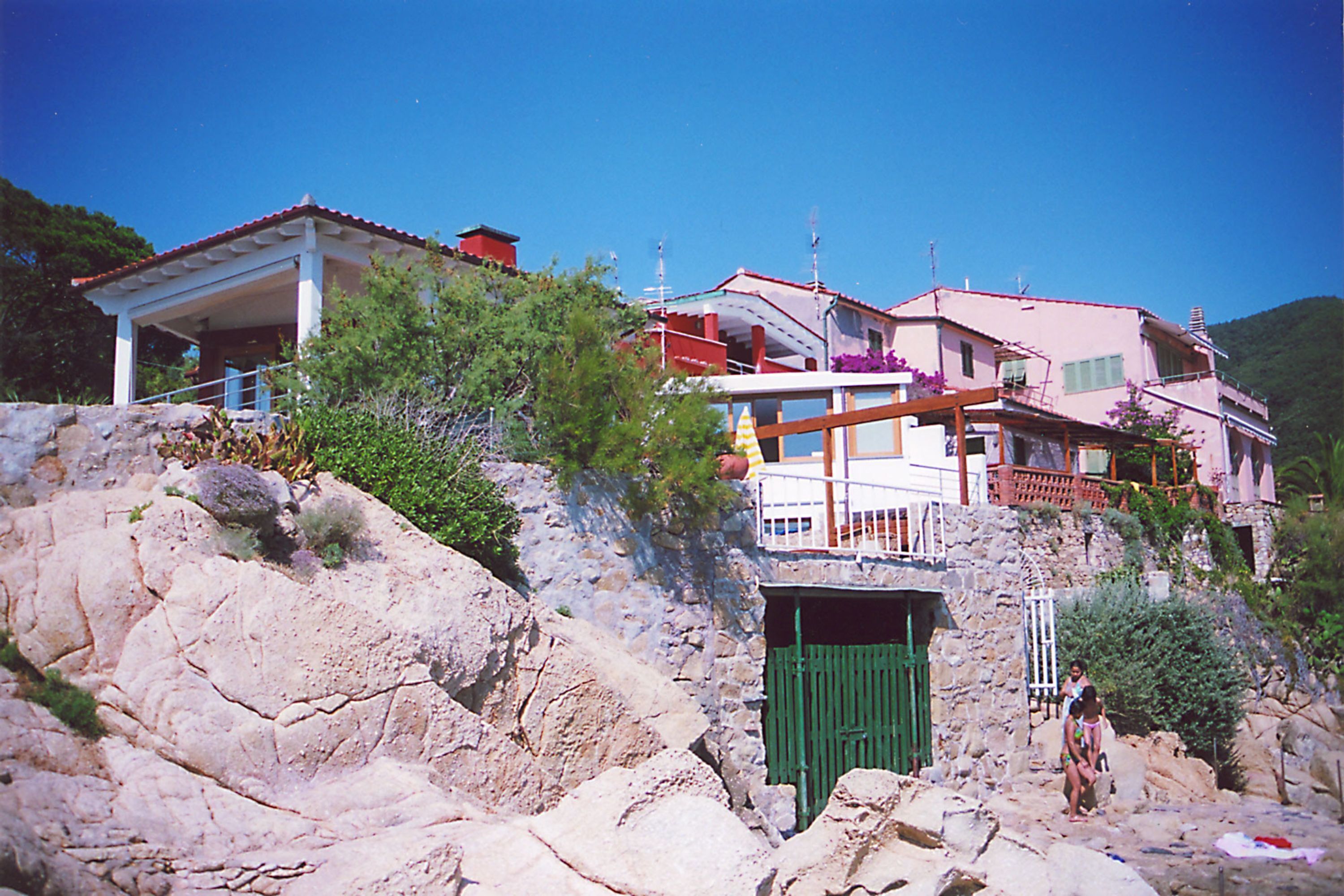 A coastal building with a stone facade, a green door, and a balcony with a railing.