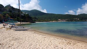 Une plage avec des bateaux, une eau cristalline et une chaîne de montagnes en arrière-plan.
