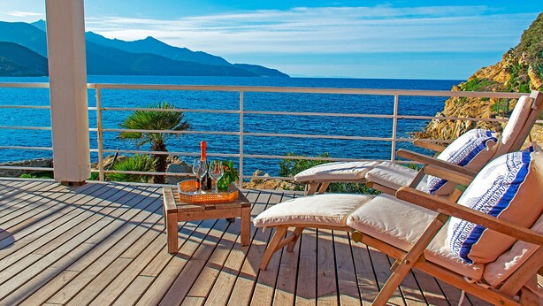 Une terrasse en bois avec des chaises longues et une table sur laquelle se trouvent une bouteille et des verres.