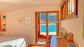 Une chambre à coucher comprenant un lit, un bureau, une chaise, une fenêtre et une vue sur un balcon et l’eau.