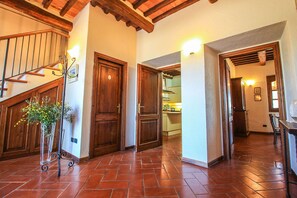 A spacious hallway with a wooden staircase, a dining area, and a kitchen visible through an open door. - Villa Campo Valerio con Grande Piscina (Scarlino)
