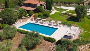 A large rectangular swimming pool with lounge chairs and umbrellas, surrounded by well-maintained gardens and a stone house with a tiled roof. - Villa Campo Valerio con Grande Piscina (Scarlino)