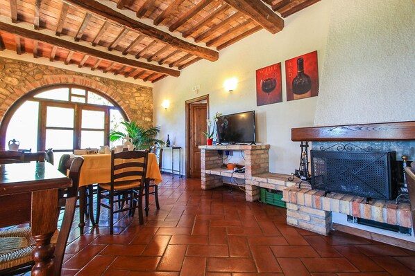 A dining area with a brick fireplace, stone arch window, and wooden ceiling beams.
