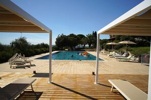 A wooden deck with a pool, lounge chairs, and umbrellas. - Villa Campo Valerio con Grande Piscina (Scarlino)