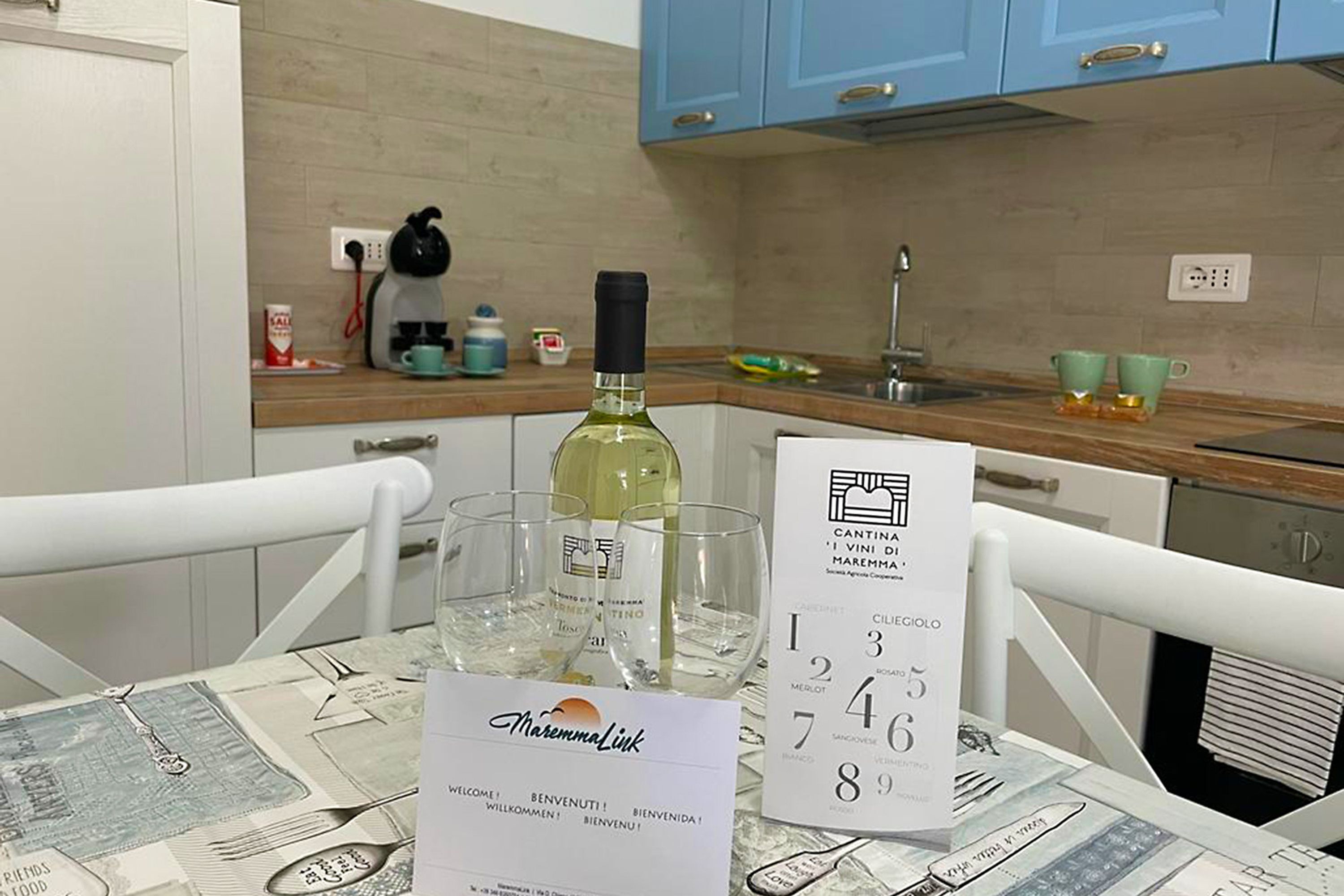 Una cocina con una mesa dispuesta para una comida, que incluye una botella de vino, copas y un menú.