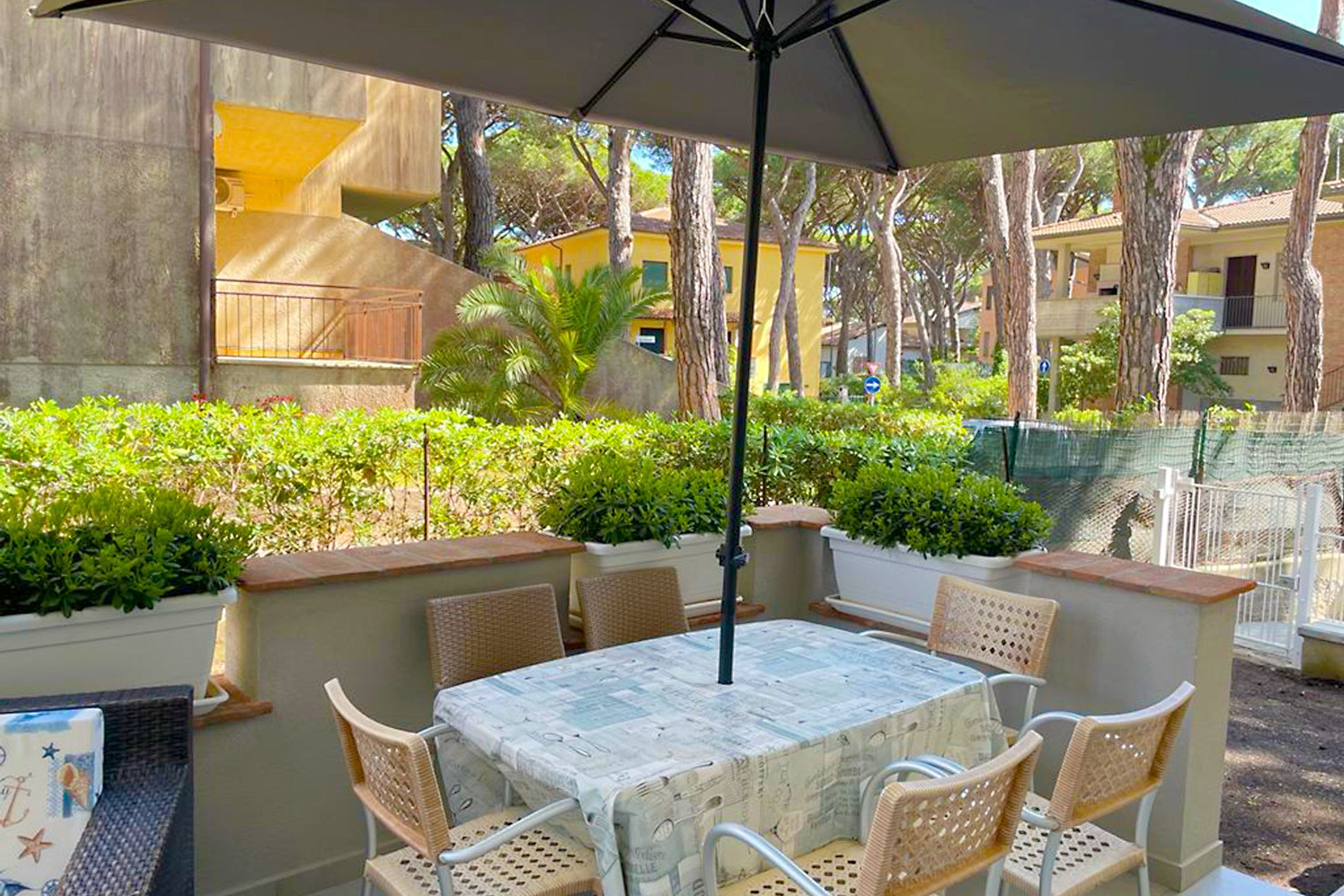 An outdoor patio with a table and chairs, surrounded by greenery and a view of buildings.