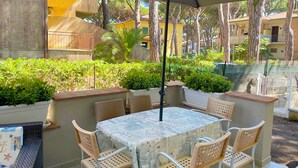 An outdoor patio with a table and chairs, surrounded by greenery and a view of buildings. - Appartamento Giglio Vicino al Mare (Grosseto)