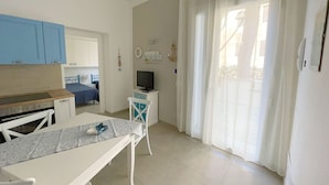 A small, bright room with a kitchenette, a dining table, a TV, and a sliding glass door to a balcony. - Appartamento Giglio Vicino al Mare (Grosseto)