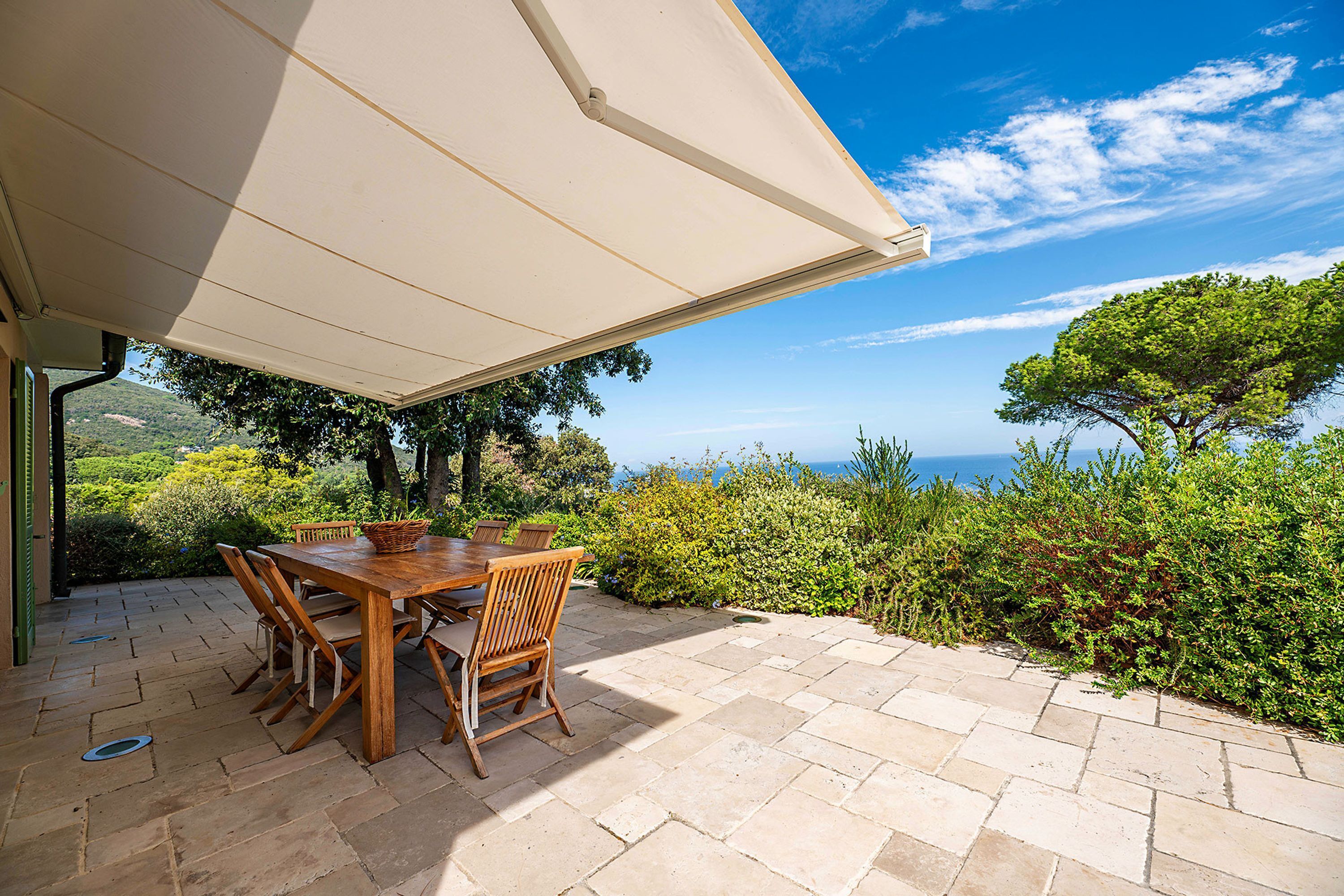 An outdoor patio with a wooden table and chairs, a white canopy, and a view of the sea.