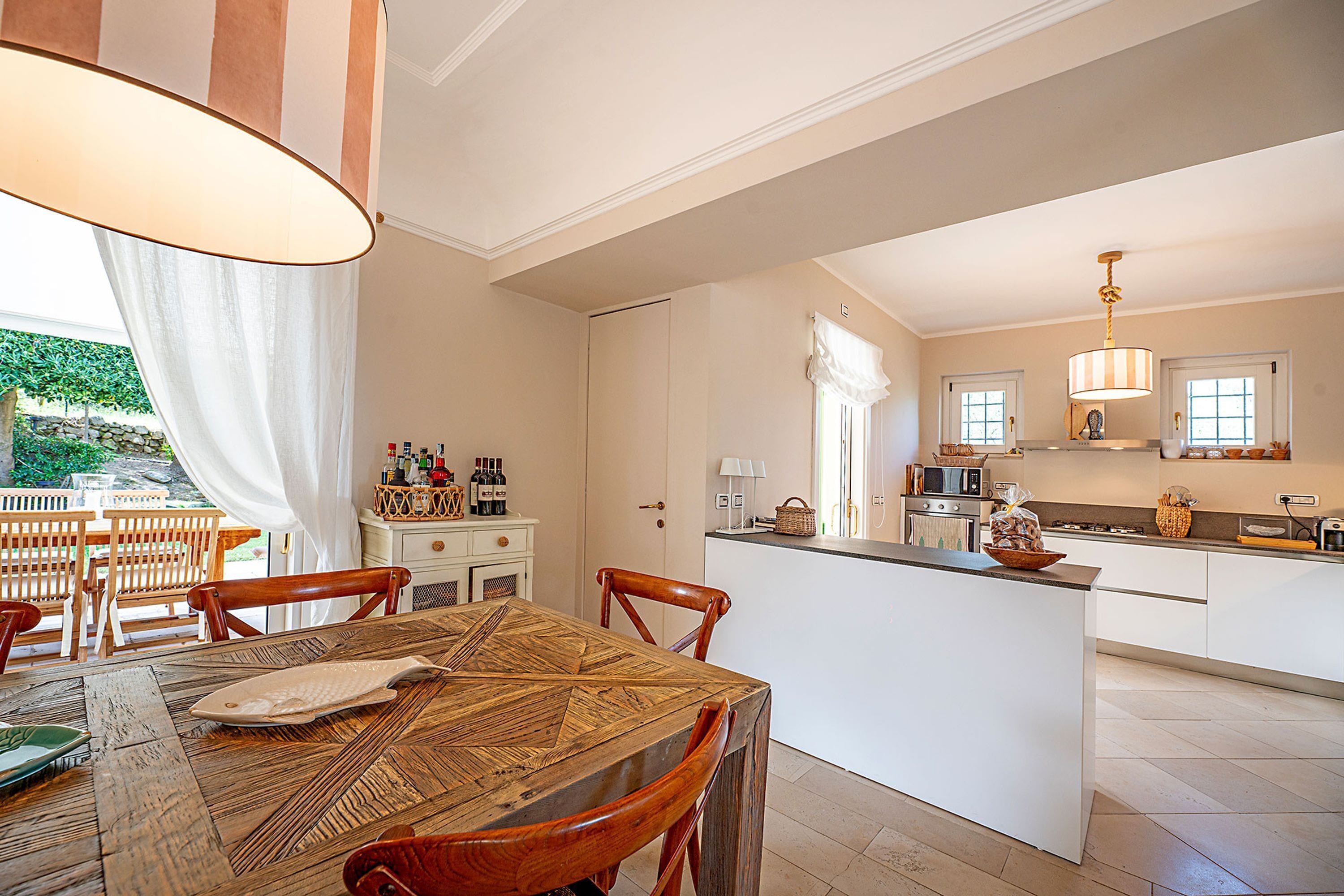 Cucina spaziosa con isola centrale, tavolo da pranzo in legno e sedie. Si apre su un giardino attraverso la finestra.
