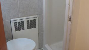 A bathroom with a toilet, a white radiator, and a shower area. - Small affordable Studio near UQAM. (Montréal)