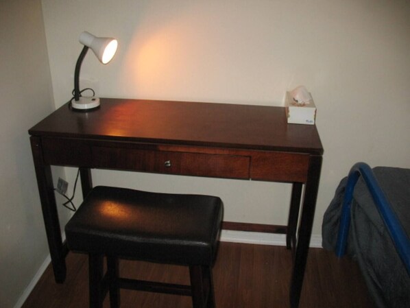 Un bureau en bois, une lampe, un banc et une boîte de mouchoirs accrochée au mur.
