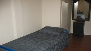 A single bed with a grey patterned bedspread and blue headboard in a room with wooden flooring and a dresser. - Small affordable Studio near UQAM. (Montréal)