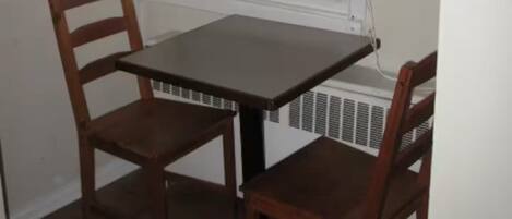 A corner room with a small table and two chairs, a window, and a radiator.