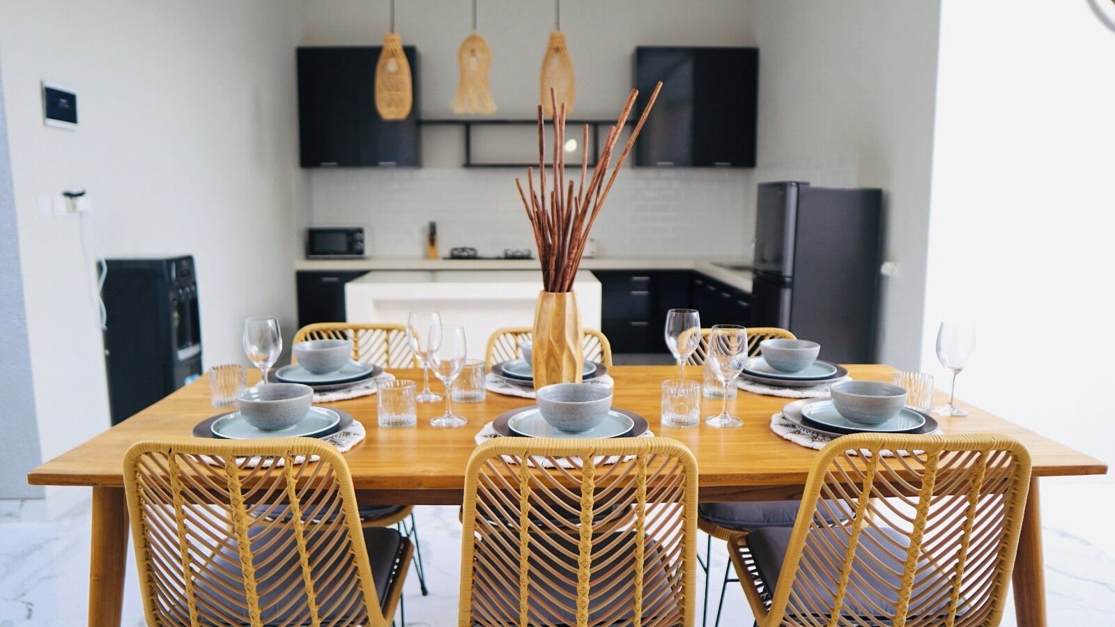Un comedor con una mesa de madera dispuesta para seis personas, rodeada de sillas de mimbre.