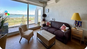 A living room with a sofa, armchair, coffee table, and a lamp. There is a view of the sea through large windows.