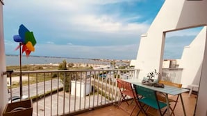A balcony with a table and chairs, a pinwheel, and a view of a coastal area.
