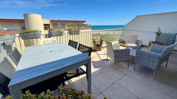 A rooftop patio with a table and chairs, potted plants, and a view of the ocean.