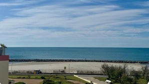 A beach view with a clear sky, a sandy shore, and a rocky breakwater.