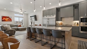A modern kitchen with grey cabinets, a stainless steel refrigerator, and a bar area with stools. - Canyon Country Oasis: Desert Color Lagoon + Beaches (St. George)