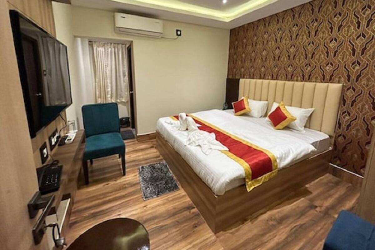 A hotel room with a bed, a desk, a chair, a television, and a patterned wall.