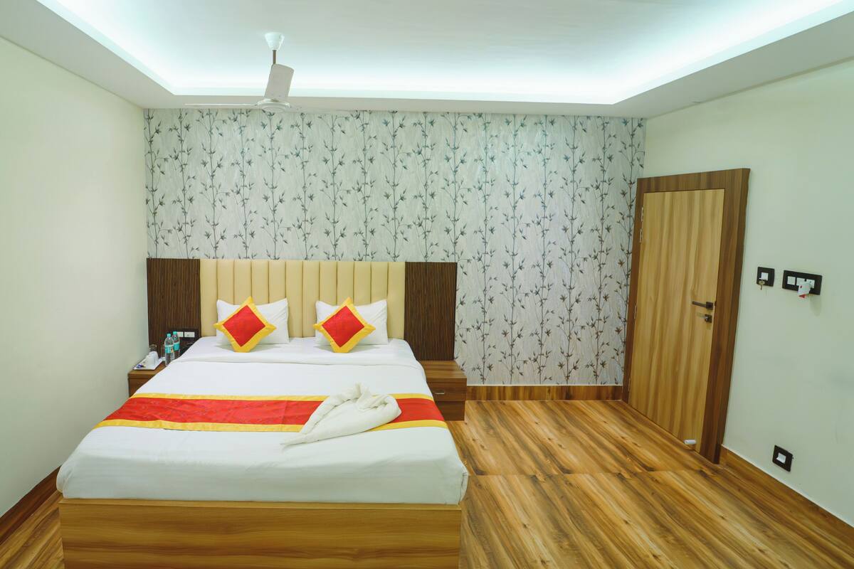 A neatly arranged hotel room with a large bed, a wooden floor, a ceiling fan, and a floral wallpaper.