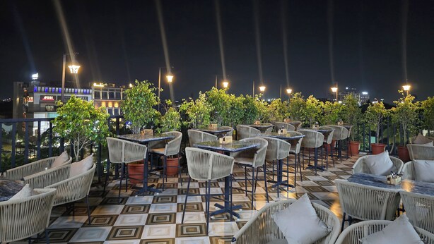 An outdoor seating area with wicker chairs and tables, potted plants, and a patterned floor. - Hotel Royal Orbit  (Bhubaneshwar)
