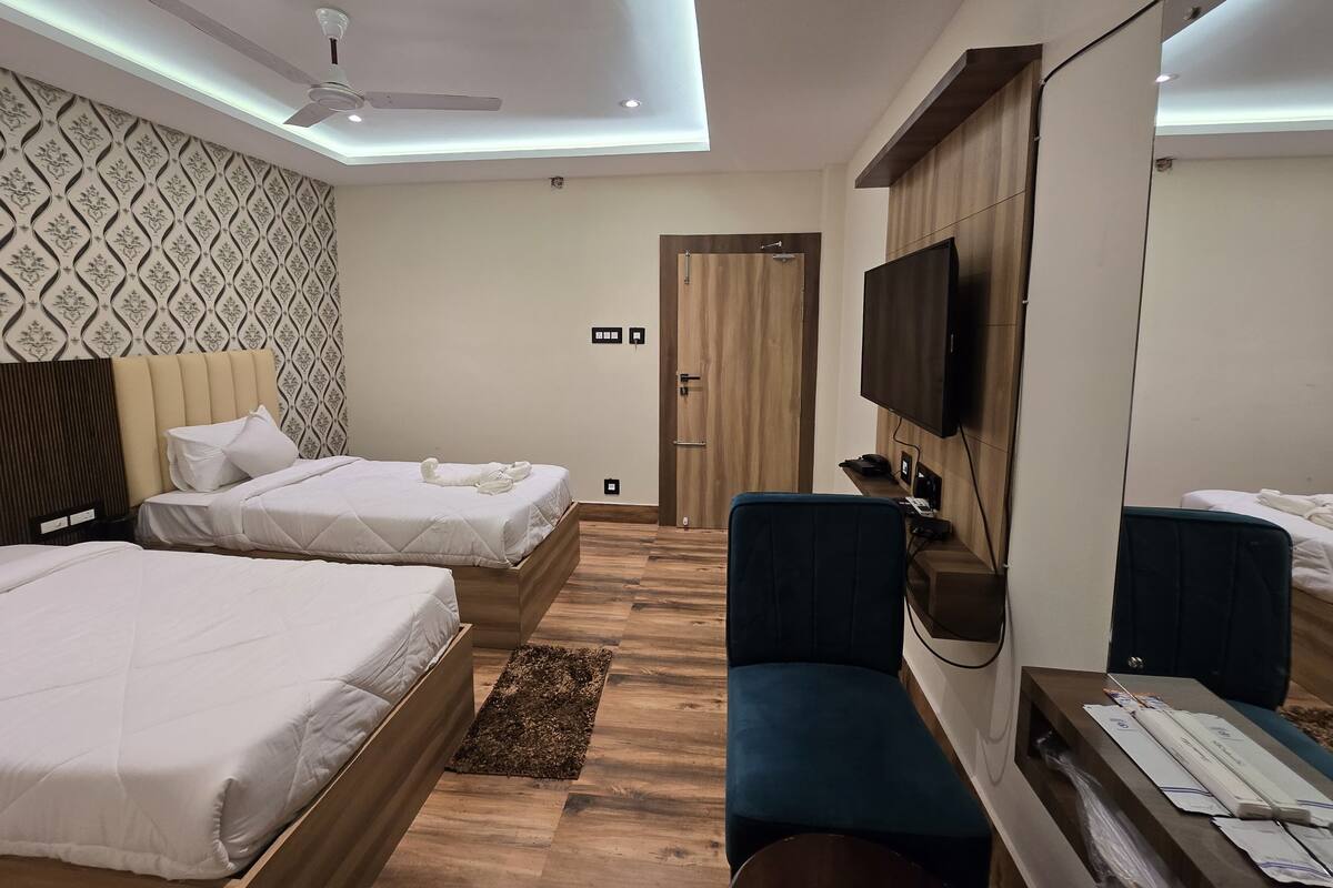 A modern hotel room with two beds, a desk, a chair, a TV, and a ceiling fan.