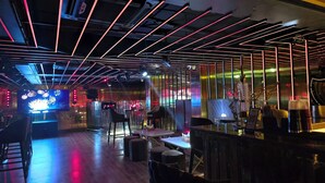 A modern bar with a high ceiling, neon lighting, and a large TV screen. - Hotel Royal Orbit  (Bhubaneshwar)