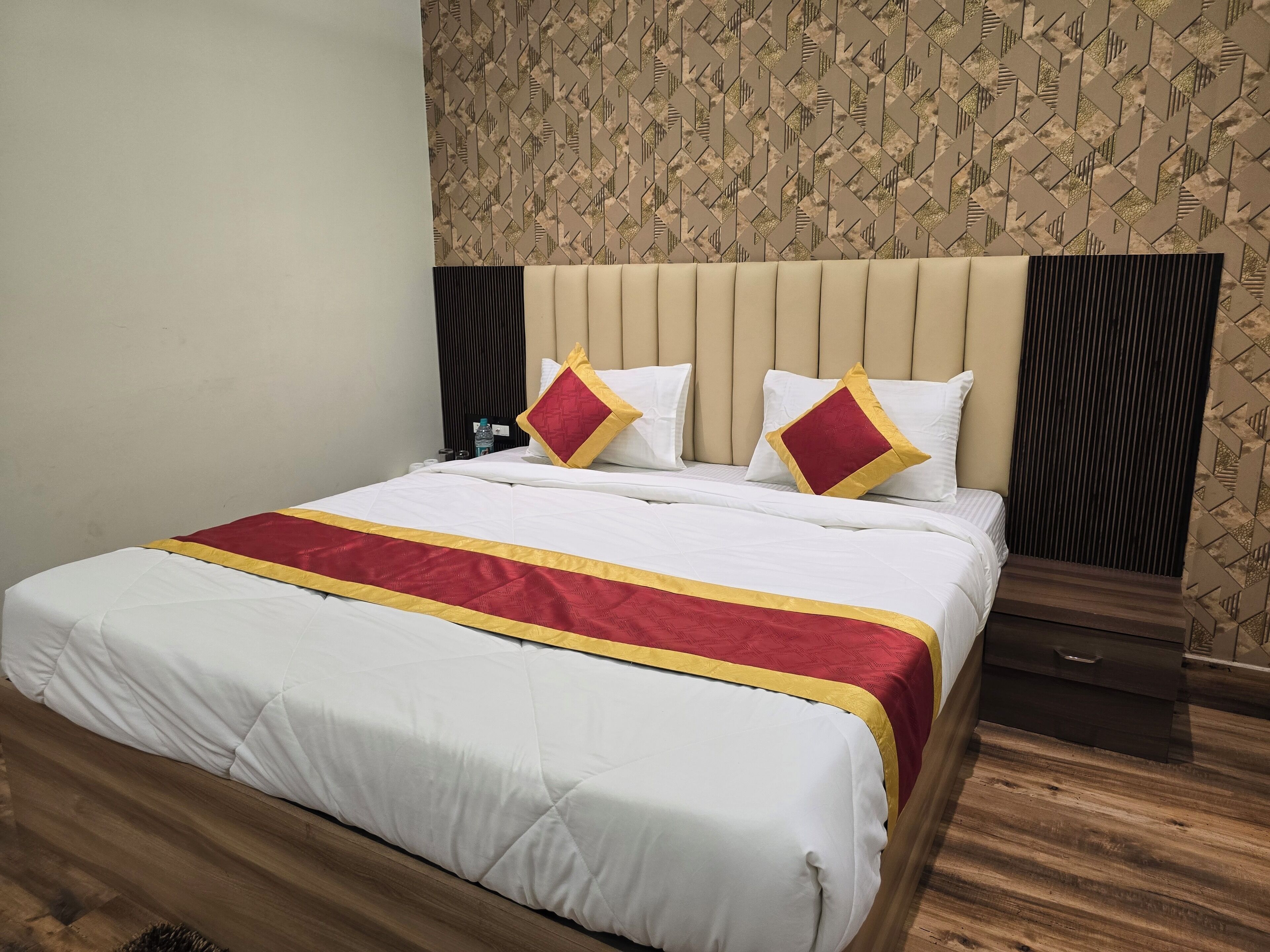 A hotel room with a large bed, a headboard, a wooden floor, and a patterned wallpaper.