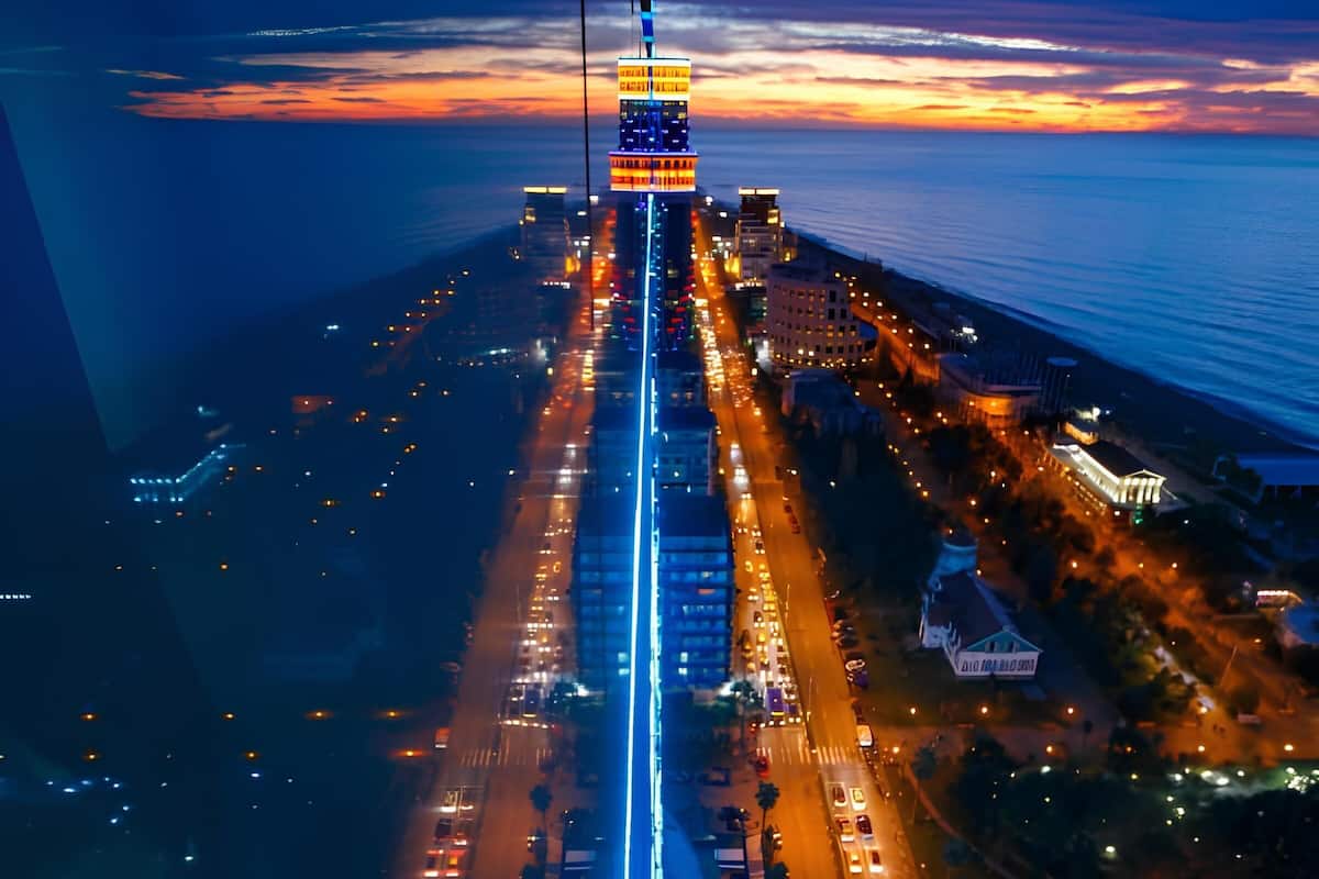 An aerial view of a cityscape at dusk with illuminated buildings and a busy road.