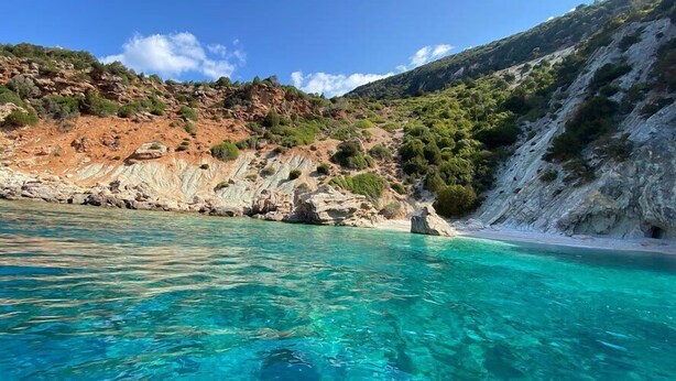 Een kustlandschap met helder turquoise water, rotsachtige kliffen en een strand.