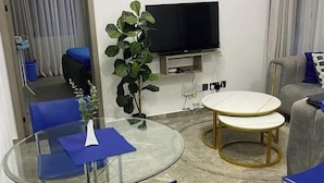Un salon moderne avec une table à manger en verre, des chaises bleues, une table basse ronde, un téléviseur à écran plat fixé au mur et une plante en pot.