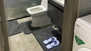 Une salle de bain compacte comprenant des toilettes, une douche en verre, un lavabo et un lave-linge LG blanc.