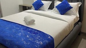 Un lit bien fait, avec une couverture bleue, des oreillers blancs et une tête de lit grise.