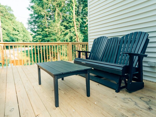 A wooden deck with a black Adirondack chair and a matching table.