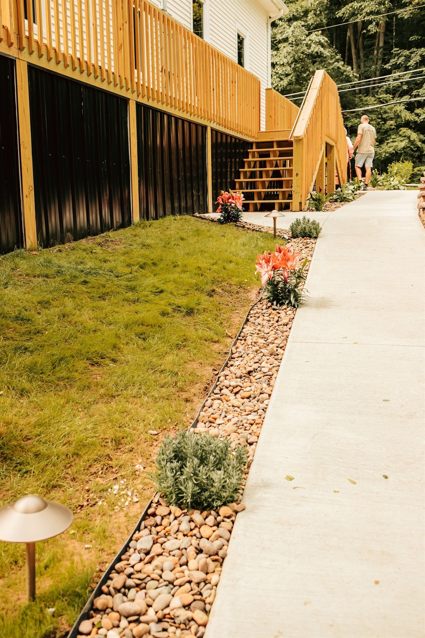 Ein gepflegter Garten mit Holzzaun, einem Betonweg und einer kleinen Brücke, die zu einem Haus führt.