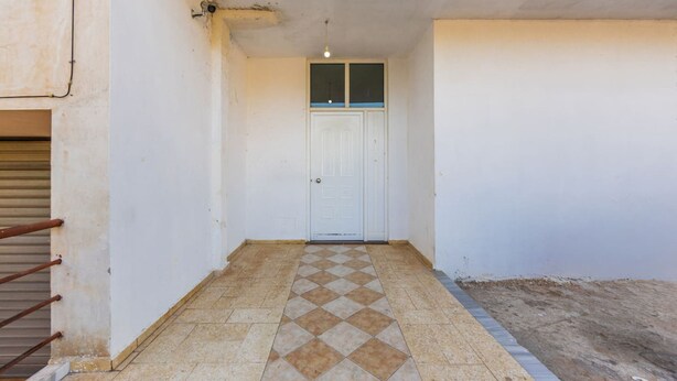 Un pasillo estrecho con piso de baldosas que conduce a una puerta blanca.